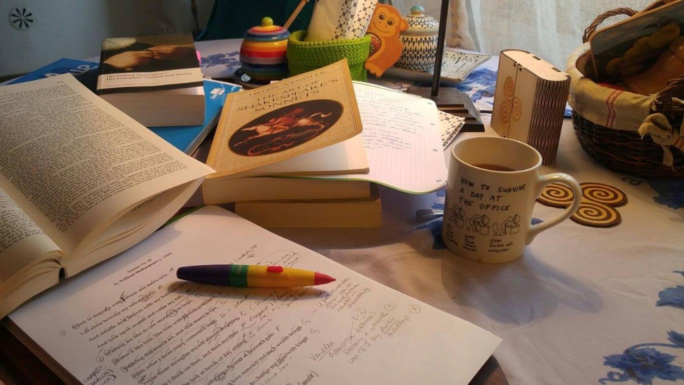 Picture of a teacher's "work from home" desk, showing books, notes, a drink, etc.